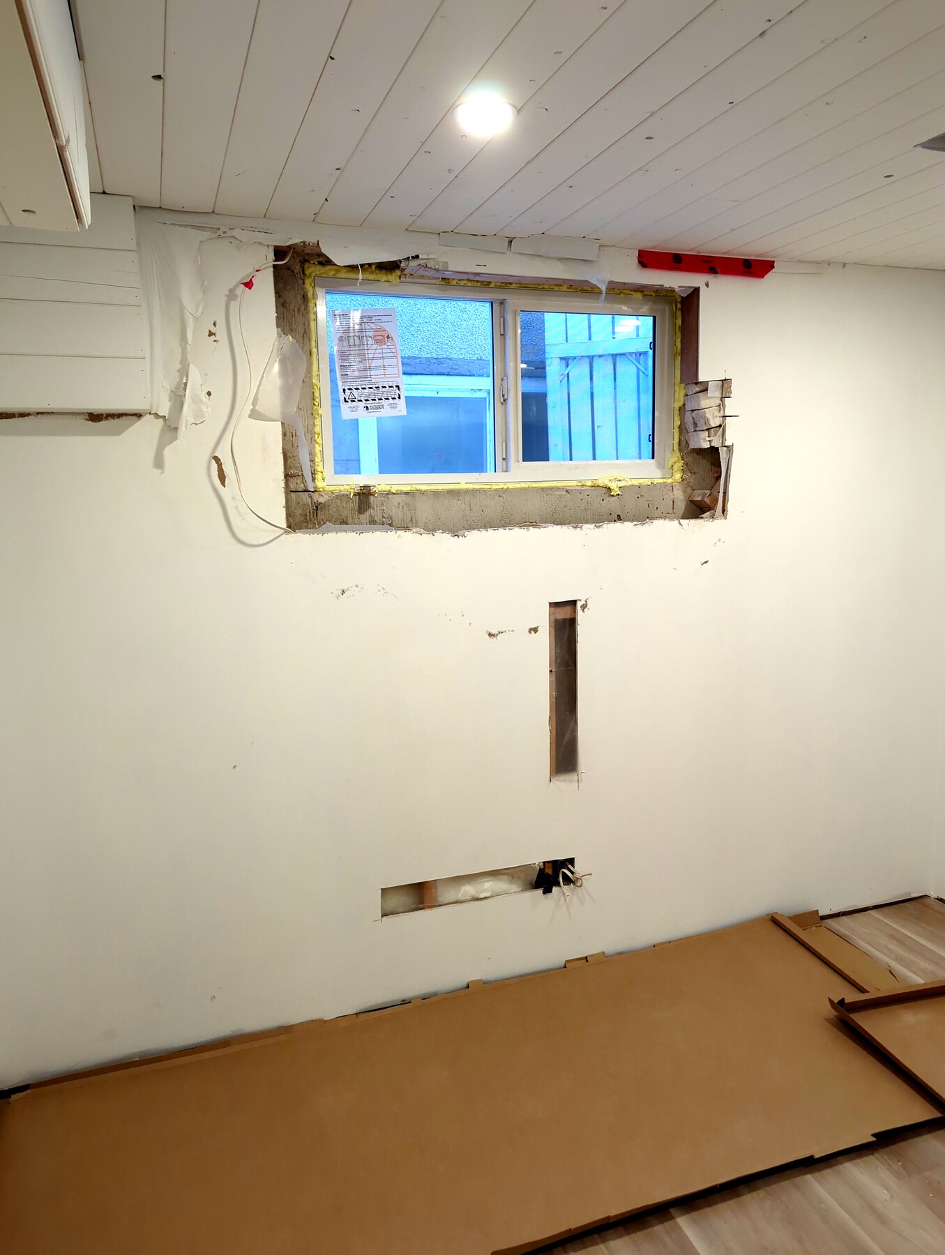 Basement room with unfinished ceiling and wall work around a window