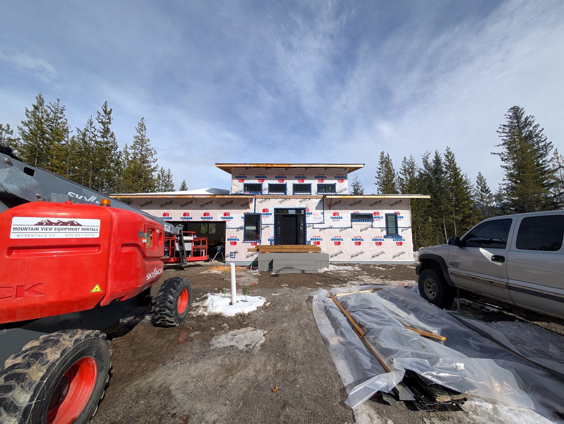 Active new-build exterior with roofline, equipment, and building wrap visible