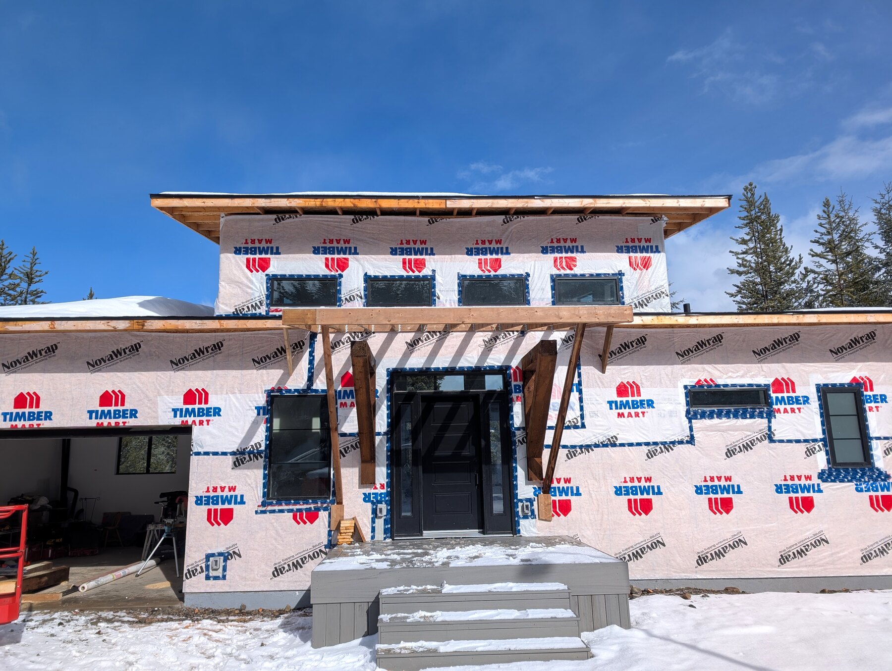 New-build exterior with wrapped walls, roof edges, and front entry work underway