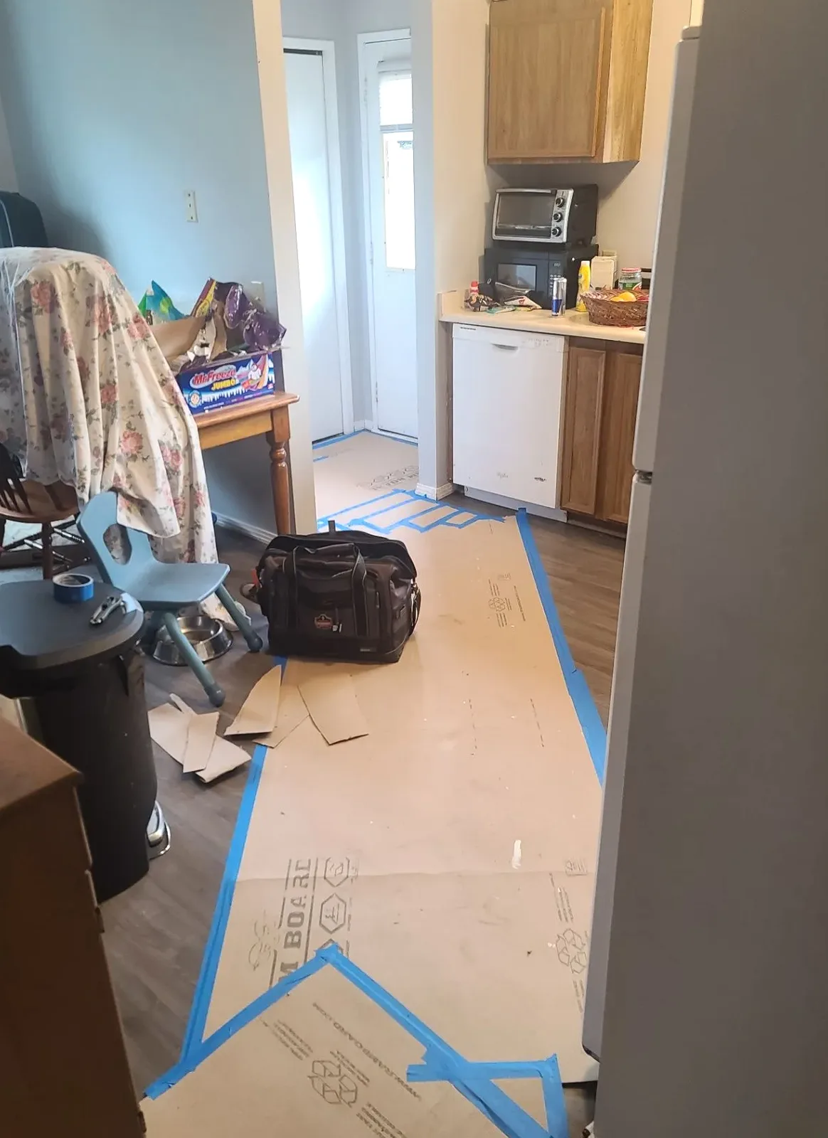 Kitchen with cabinet and appliance area visible above taped protective floor covering