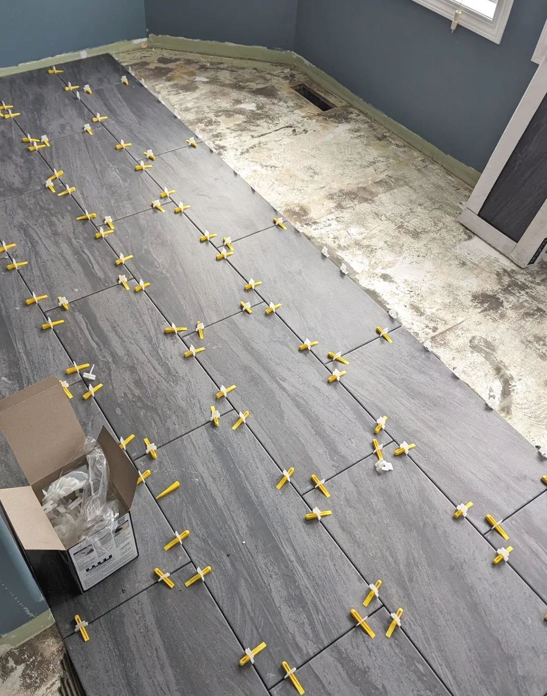 Large-format grey wood-look floor tile being laid with levelling clips and spacers